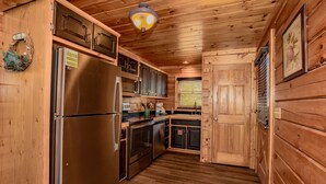 A wooden cabin interior with a stainless steel refrigerator, wooden cabinets, a built-in oven, and a window with blinds. - 🌙 Midnight Wonder 🏔️ Twinkling Valley Lights, Hot Tub & Resort Pool (Sevierville)