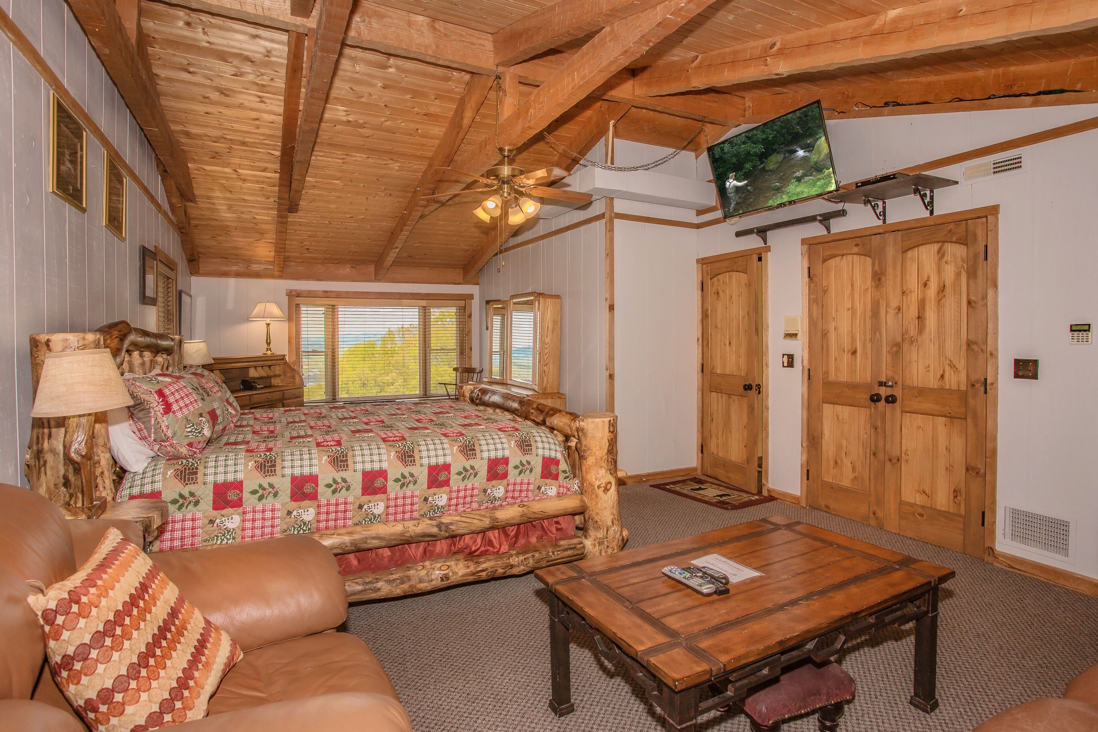 Une chambre confortable avec un lit, des meubles en bois, un ventilateur de plafond et un téléviseur fixé au mur.