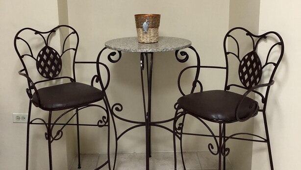 Un petit coin repas avec deux chaises en métal et une table ronde, agrémenté d’une décoration murale au-dessus.
