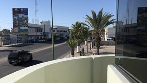 Un balcon donnant sur une rue, des palmiers et un immeuble avec une enseigne.