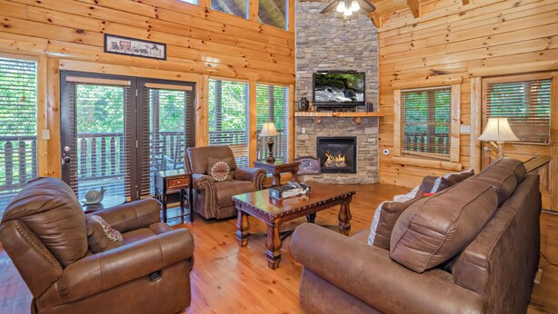 A log cabin interior with a stone fireplace, leather furniture, and a television. - Bearly Wet: Indoor Pool, Mtn Views! Hot tub, Wifi, Game Room, near attractions (Sevierville)