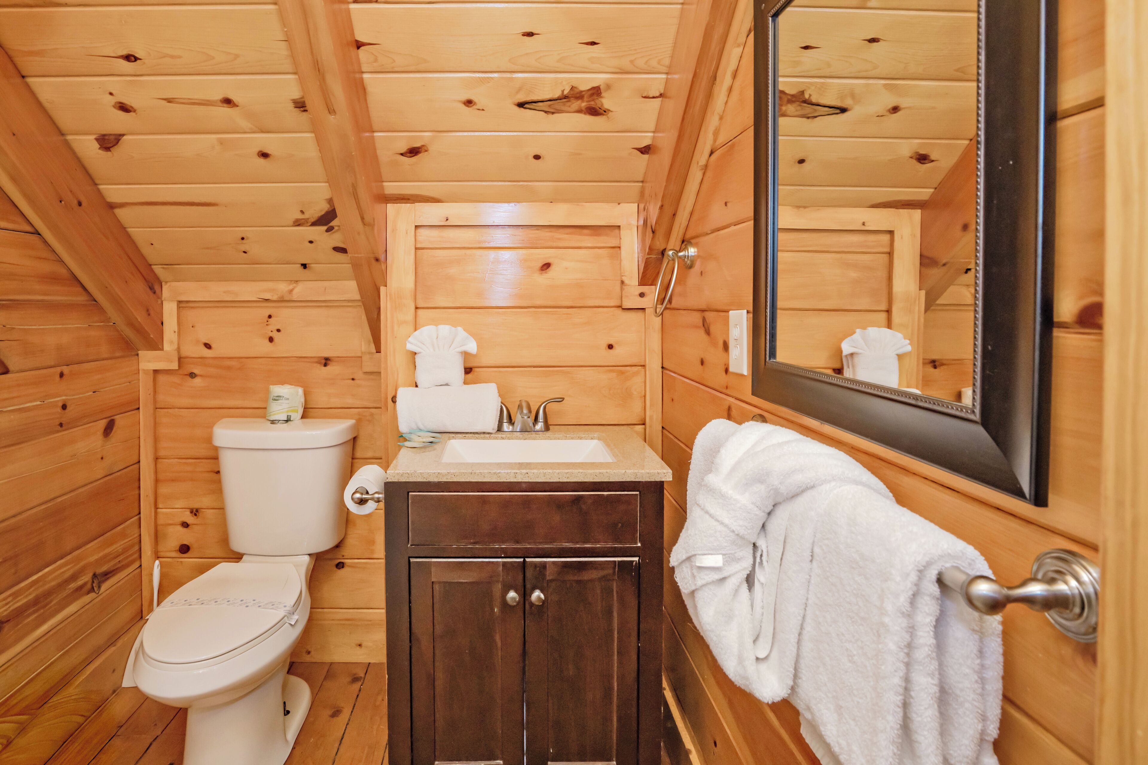 Un baño de cabaña de madera con inodoro, lavamanos, armario y toallero.