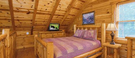 Une chambre située dans un chalet en rondins, avec un lit en bois, un téléviseur posé sur un meuble, une fenêtre avec des stores et une lampe sur une table de chevet.