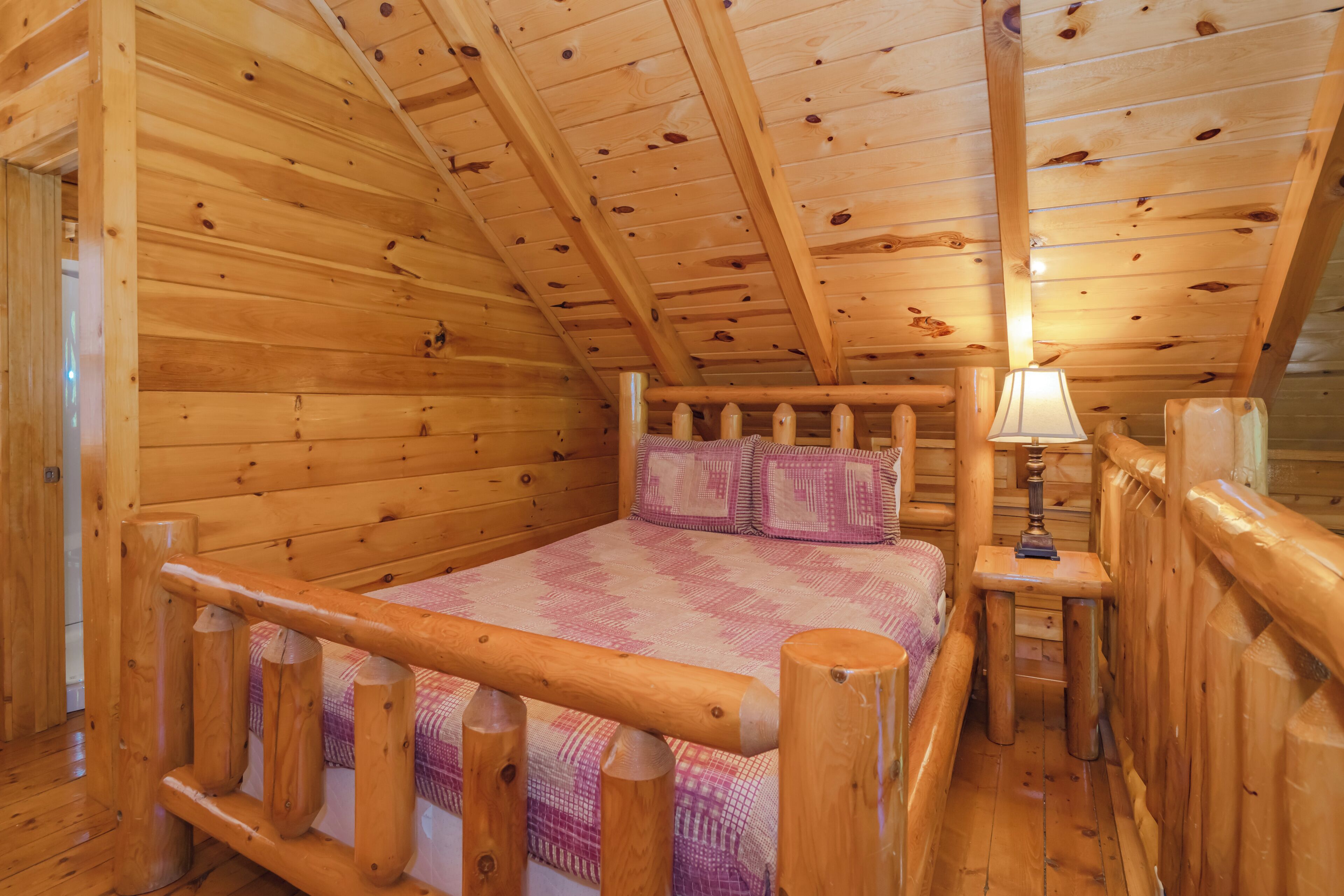 A wooden cabin bedroom with a bed, pillows, a nightstand, and a lamp.