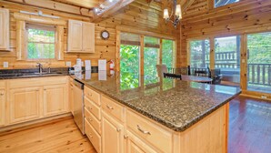 A wooden cabin interior with a kitchen featuring granite countertops, wooden cabinets, and a dining area with a table and chairs. - Bearly Wet: Indoor Pool, Mtn Views! Hot tub, Wifi, Game Room, near attractions (Sevierville)