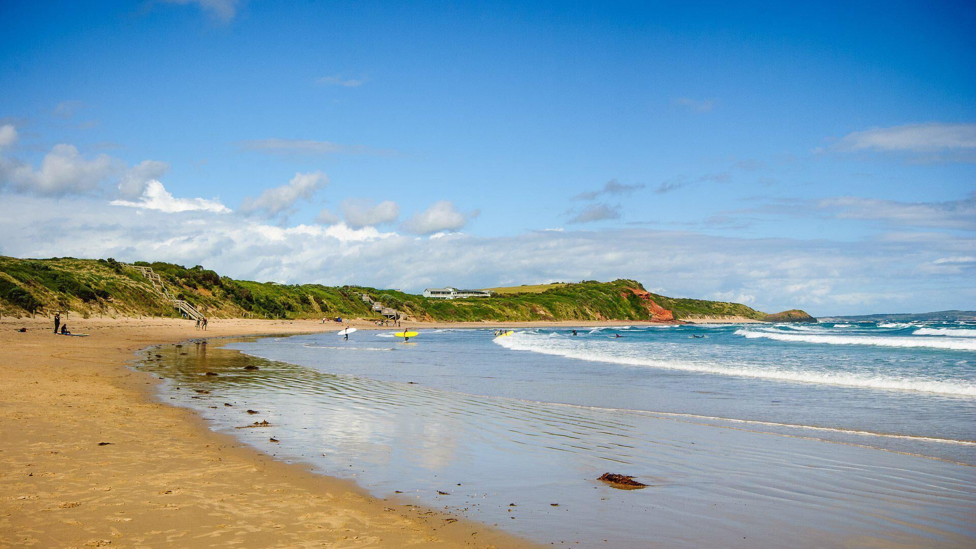 Ein Strand mit Sandküste, Wellen und einem grasbewachsenen Hügel im Hintergrund.