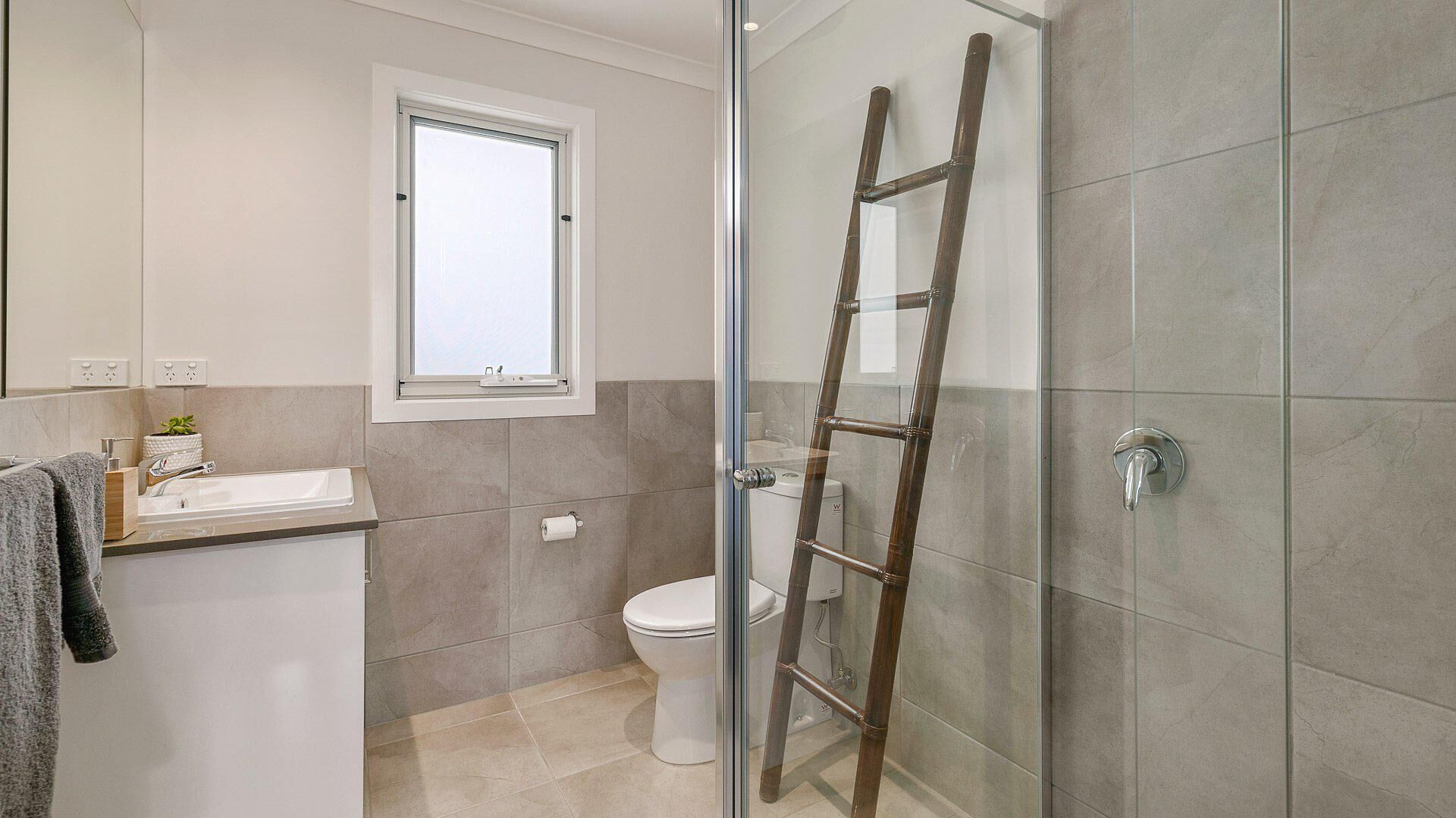 Une salle de bain comprenant des toilettes, un lavabo, une fenêtre et une douche en verre avec une échelle en bois.