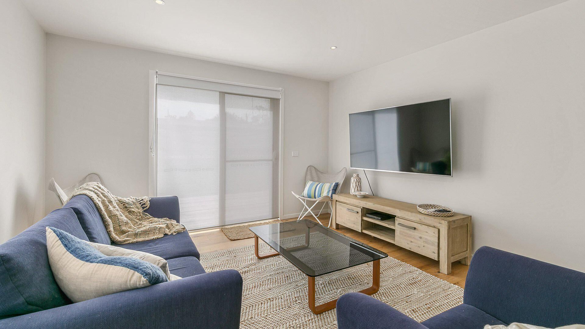 A modern living room with a sofa, coffee table, and a flat-screen TV mounted on the wall.