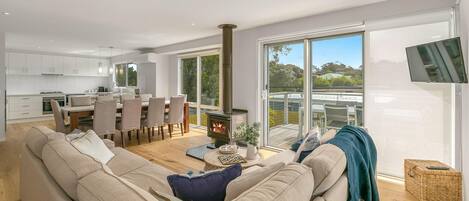 A modern living room with a sofa, a dining area with chairs, a kitchen, and a large window with a view.