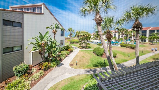 A modern building with a flat roof and large windows, surrounded by well-maintained lawns and palm trees. - Gulf/Pool View End Unit with extra balcony! (Sarasota)