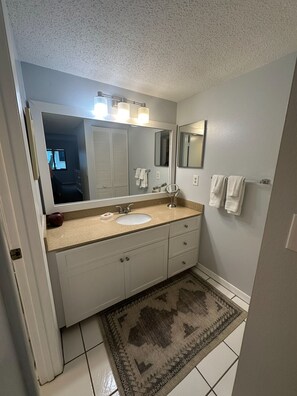 A bathroom with a white vanity, a sink, a large mirror, and a patterned rug on the floor.
