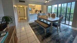 A modern kitchen with white cabinets, a dining area with a wooden table and chairs, and a large window offering a view of the city. - Gulf/Pool View End Unit with extra balcony! (Sarasota)