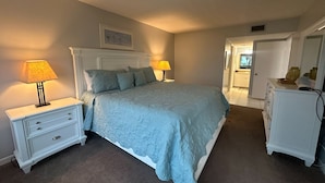 A bedroom with a bed, two bedside tables, a dresser, and a door leading to another room. - Gulf/Pool View End Unit with extra balcony! (Sarasota)