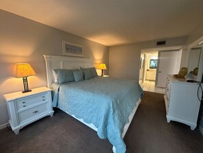 Ein Schlafzimmer mit einem Bett, zwei Nachttischen, einer Kommode und einer Tür zu einem anderen Raum.