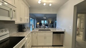 A modern kitchen with white cabinets, a stainless steel dishwasher, and a granite countertop. - Gulf/Pool View End Unit with extra balcony! (Sarasota)