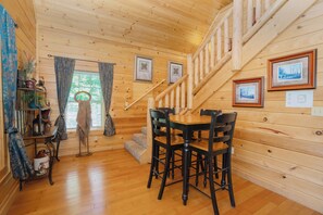A wooden interior with a staircase, a dining table with chairs, and framed pictures on the walls.