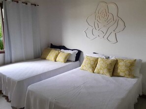 Zwei Einzelbetten mit weißen Laken und gemusterten Kissen, ein großes Blumenbild an der Wand und ein Fenster mit weißen Vorhängen.