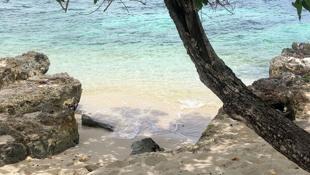 A beach with clear turquoise water, sandy shore, and large rocks. - Heaven-Can-Wait @ Point Village (Negril)