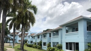 A row of light blue buildings with balconies, surrounded by lush greenery and palm trees. - Heaven-Can-Wait @ Point Village (Negril)