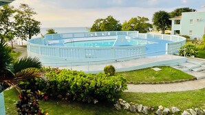 A circular pool with a blue deck, surrounded by a low stone wall and lush greenery. - Heaven-Can-Wait @ Point Village (Negril)