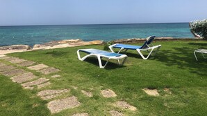 A grassy area with two lounge chairs facing the ocean. - Heaven-Can-Wait @ Point Village (Negril)