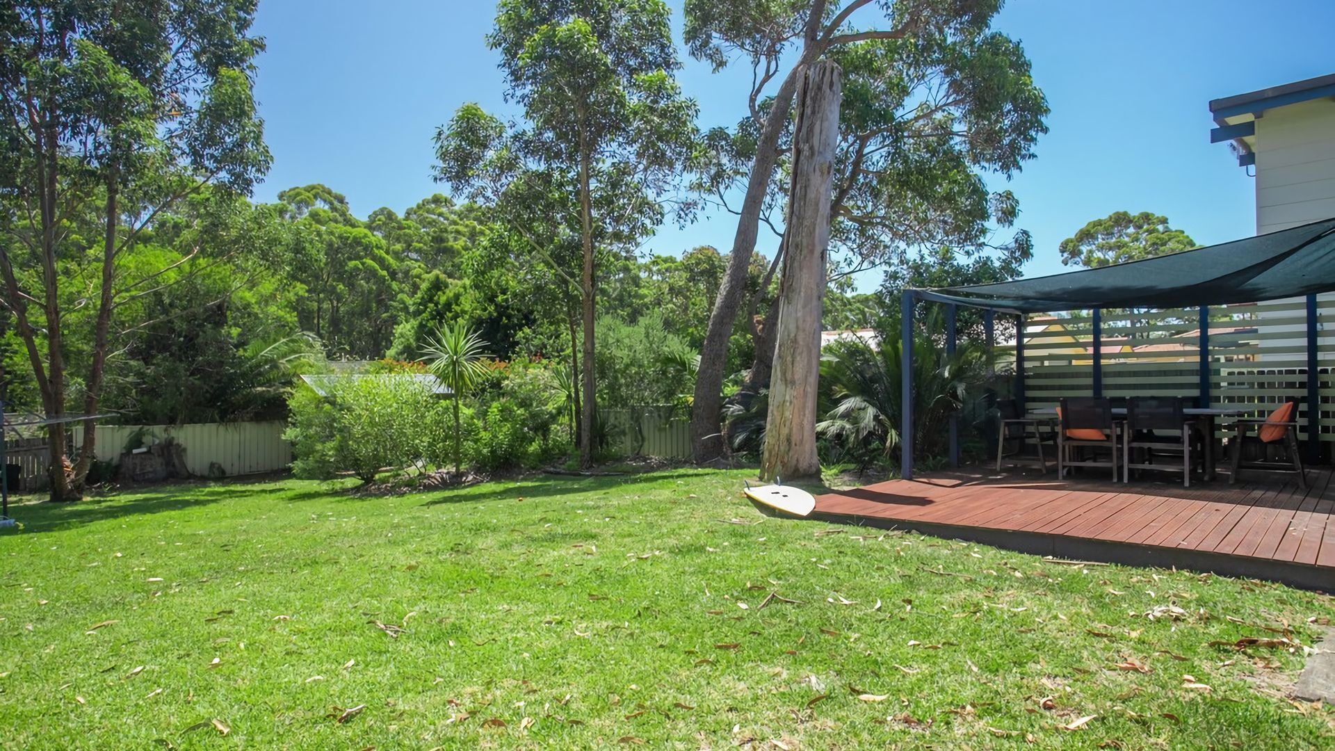 A backyard with a wooden deck, a covered seating area, and a variety of trees and shrubs.