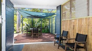 Ein überdachter Patio-Bereich mit Tisch und Stühlen, umgeben von einem Bambuszaun und einer blauen Wand.
