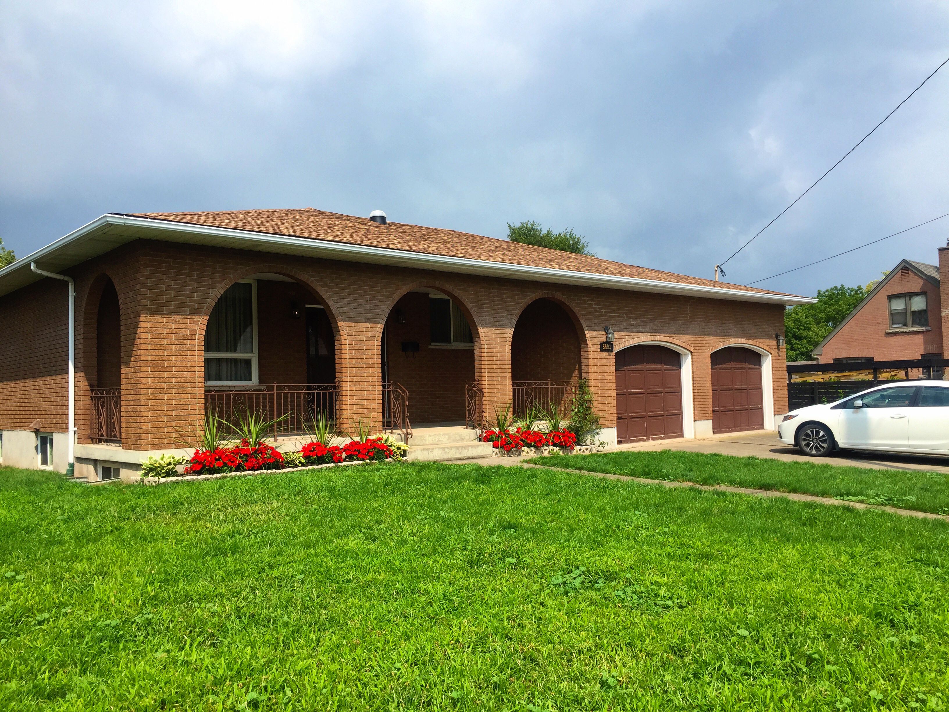 A two-story brick house with a front porch, a garage, and a well-maintained lawn.