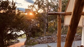 A rustic outdoor setting with a wooden structure, possibly a gazebo, surrounded by trees and a stone wall. -  Romantic Lakefront Escape: Massage, Yoga, Winery, Kayaks, SUPs, Krause Springs! (Spicewood)