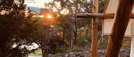 A rustic outdoor setting with a wooden structure, possibly a gazebo, surrounded by trees and a stone wall.
