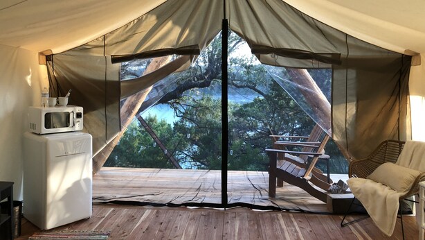 A tent with a view of trees, a microwave, a chair, and a small table. -  Romantic Lakefront Escape: Massage, Yoga, Winery, Kayaks, SUPs, Krause Springs! (Spicewood)