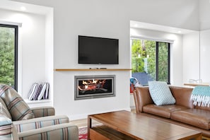 A modern living room with a fireplace, a flat-screen TV mounted above it, and a leather sofa with a throw blanket. - Alto Vista (Lorne)