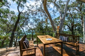 Une terrasse extérieure avec une table en bois et deux bancs en bois, entourée d’arbres.