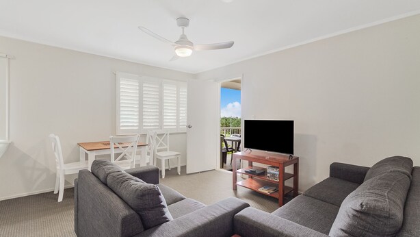 A living room with grey sofas, a wooden coffee table, a TV on a stand, and a dining area with white chairs and a table.