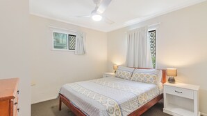 A bedroom with a bed, two bedside tables, a ceiling fan, and two windows with curtains.
