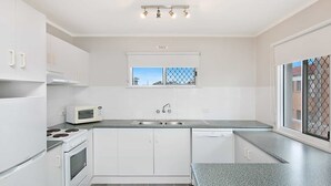 A modern kitchen with white cabinets, a microwave, a stove, a sink, and a window with a view.