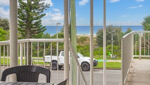 A view from a balcony overlooking a beach with a white pickup truck parked on the street.