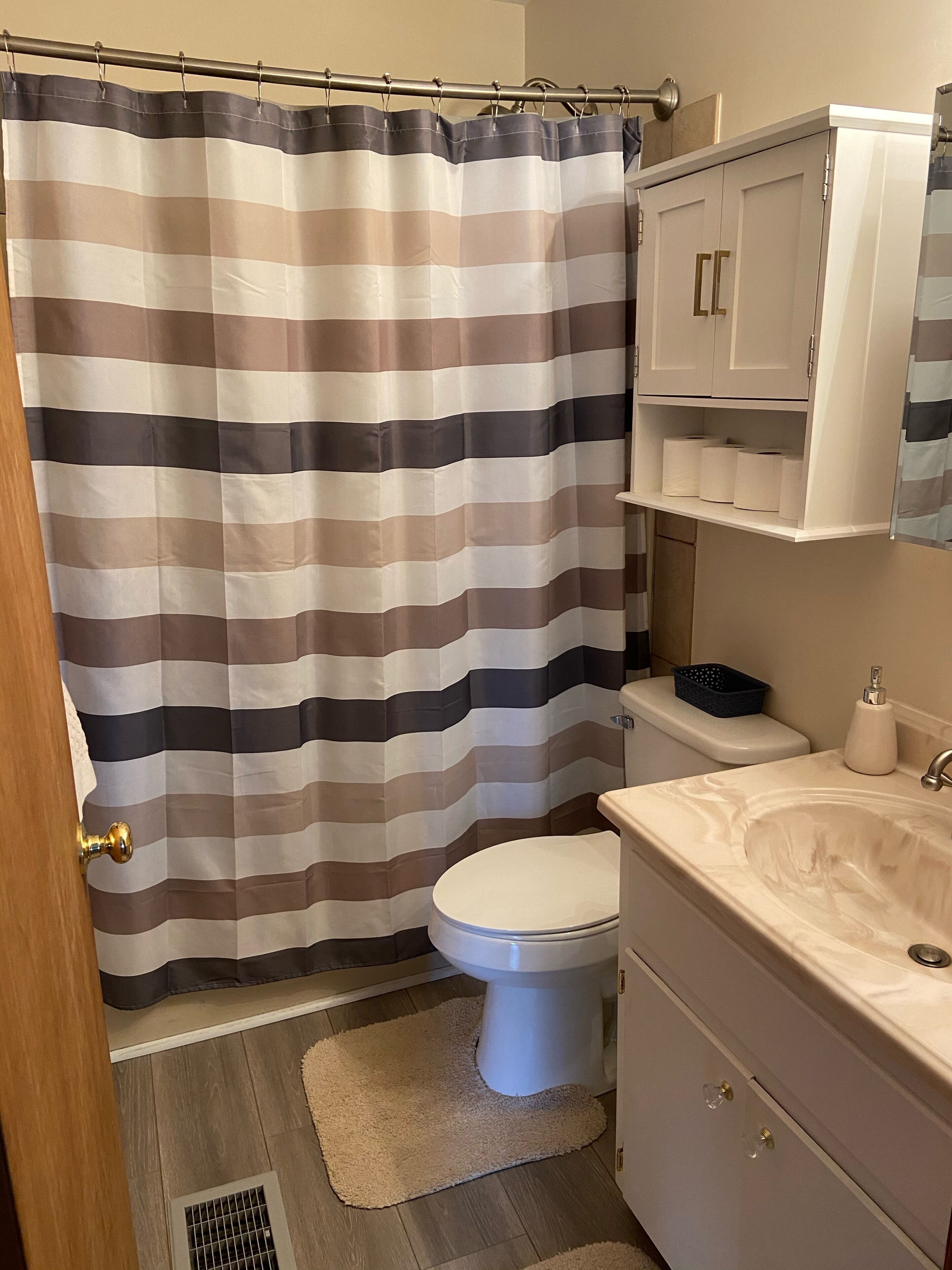A bathroom with a striped shower curtain, a toilet, a sink, and a cabinet.