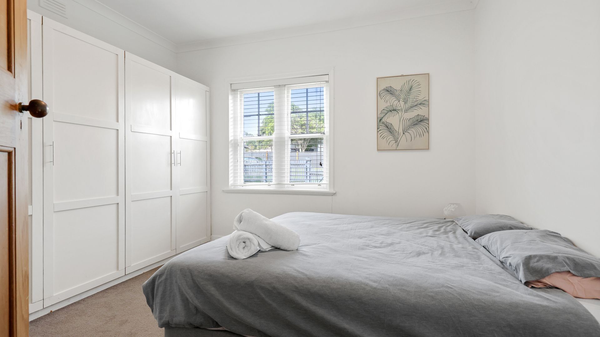 A bedroom with a bed, a window with blinds, a wardrobe, and a wall-mounted plant illustration.
