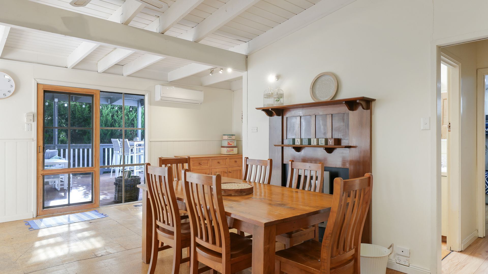 A dining area with a wooden table and chairs, a built-in shelf with a 'FAMILY' sign, and a view through a glass door to an outdoor patio.