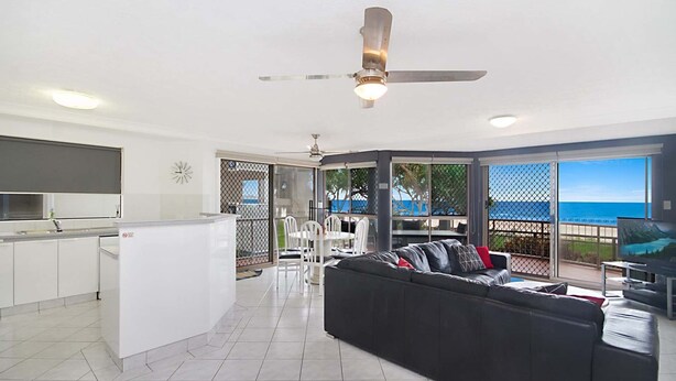 A modern kitchen with white cabinets, a dining area with a black sofa and chairs, and a large sliding glass door leading to a balcony with a view of the ocean. - Seacrest 2 - Absolute Beachfront Tugun (Tugun)
