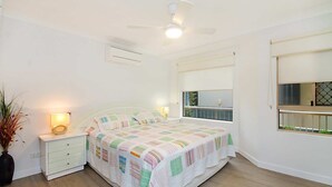 A bedroom with a bed, bedside tables, a ceiling fan, a window with a view, and a potted plant. - Seacrest 2 - Absolute Beachfront Tugun (Tugun)