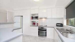 A modern kitchen with white cabinetry, a built-in oven, a microwave, and a toaster. - Seacrest 2 - Absolute Beachfront Tugun (Tugun)