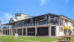 A modern building with a glass facade, a covered outdoor seating area, and a sign indicating the entrance. - Seacrest 2 - Absolute Beachfront Tugun (Tugun)