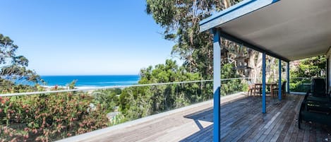 A wooden deck with a view of the ocean, a covered seating area, and a table with chairs.