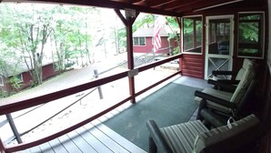 A covered porch with wooden railings, a bench, and a view of a red building and trees. - #7 Adirondack@Birchwood Cottages on Loon Lake. Family Friendly Waterfront (Chestertown)