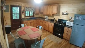 A wooden cabin kitchen with a dining table, chairs, a stove, a microwave, and wooden cabinets. - #7 Adirondack@Birchwood Cottages on Loon Lake. Family Friendly Waterfront (Chestertown)