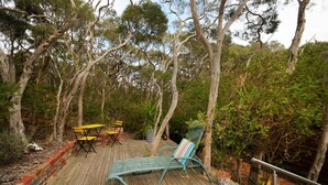 Une terrasse en bois, agréée de meubles d’extérieur, entourée d’arbres.