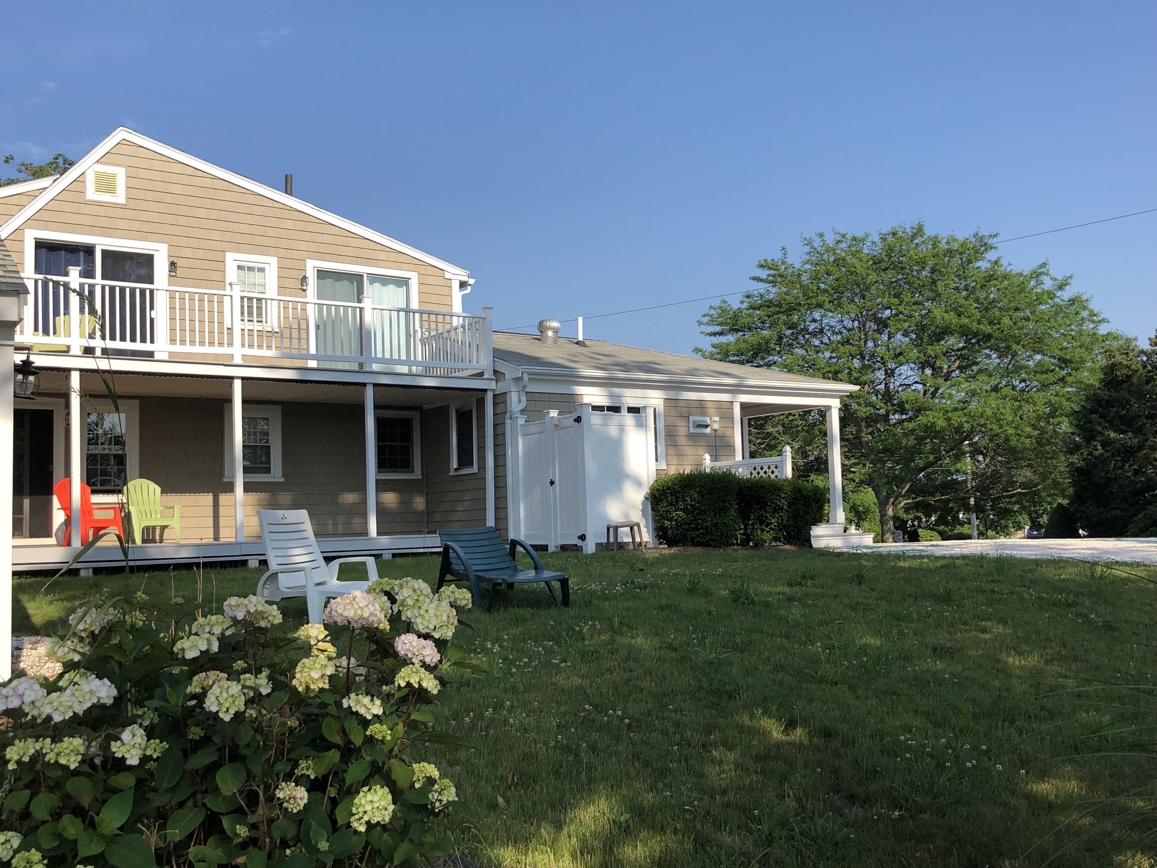 A two-story house with a balcony, a covered porch, and a well-maintained lawn with hydrangea bushes.
