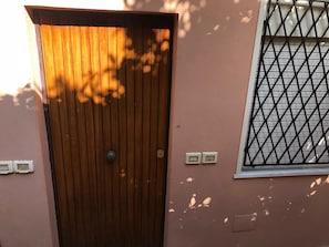 Una porta in legno con una maniglia metallica, una finestra con inferriata e due interruttori della luce fissati al muro.